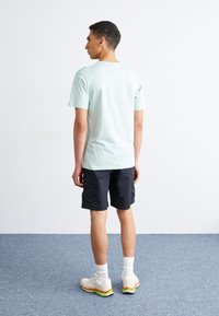 Lyseblå kortermet t-skjorte, svarte shorts, hvite joggesko med grønne og oransje aksenter, båret av en person sett fra ryggen.