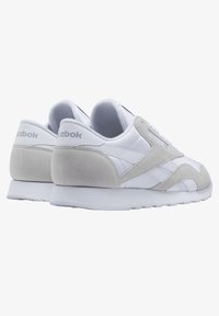 Weiße Sportschuhe mit grauen Wildlederakzenten, Schnürdesign, gepolstertem Schaft und Gummisohle; mit Reebok-Logo an der Ferse.