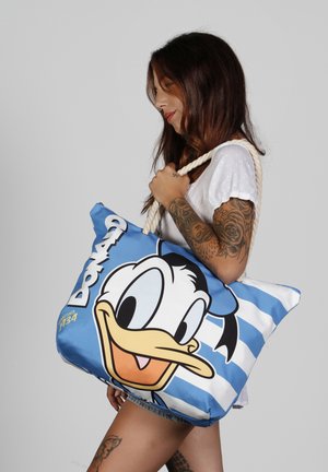 Bolsa de lona azul con un gran gráfico de Donald Duck, patrón a rayas y asas de cuerda gruesas. El texto incluye "Donald" y la fecha de establecimiento.