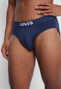 Tengerészkék Levi's alsónadrág vastag elasztikus derékkal, amelyen fehér logószöveg látható. Az anyag lágy érzetű, a fazon pedig illeszkedő, kontúros kialakítású.