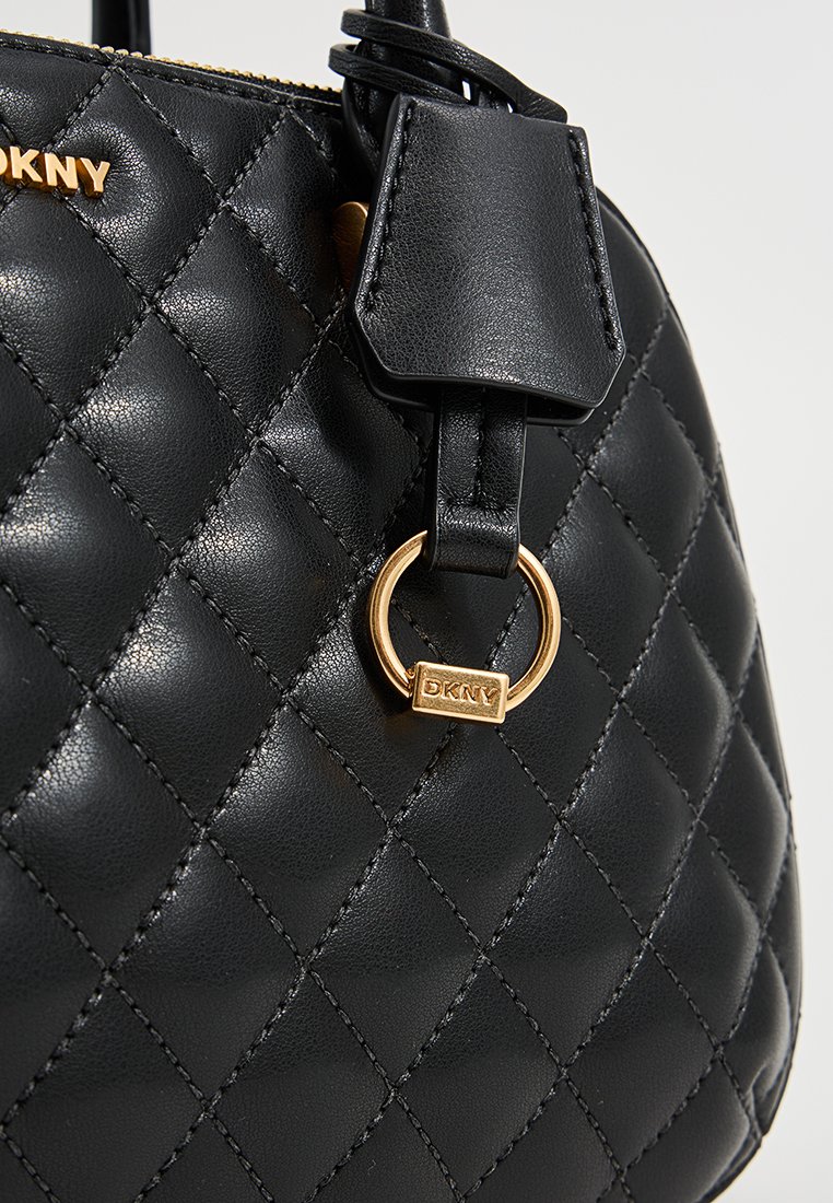 Schwarze, gesteppte Handtasche aus strukturiertem Leder. Ausgestattet mit goldfarbener Hardware, einem Anhänger mit "DKNY" und einem runden Ringakzent.