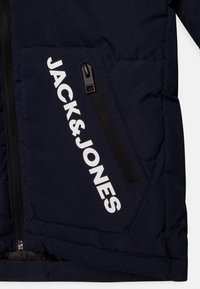 Granatowa kurtka puchowa ma kieszeń na zamek błyskawiczny z czarnym zamkiem oraz biały napis "JACK & JONES" z przodu, z pikowanym wzorem.