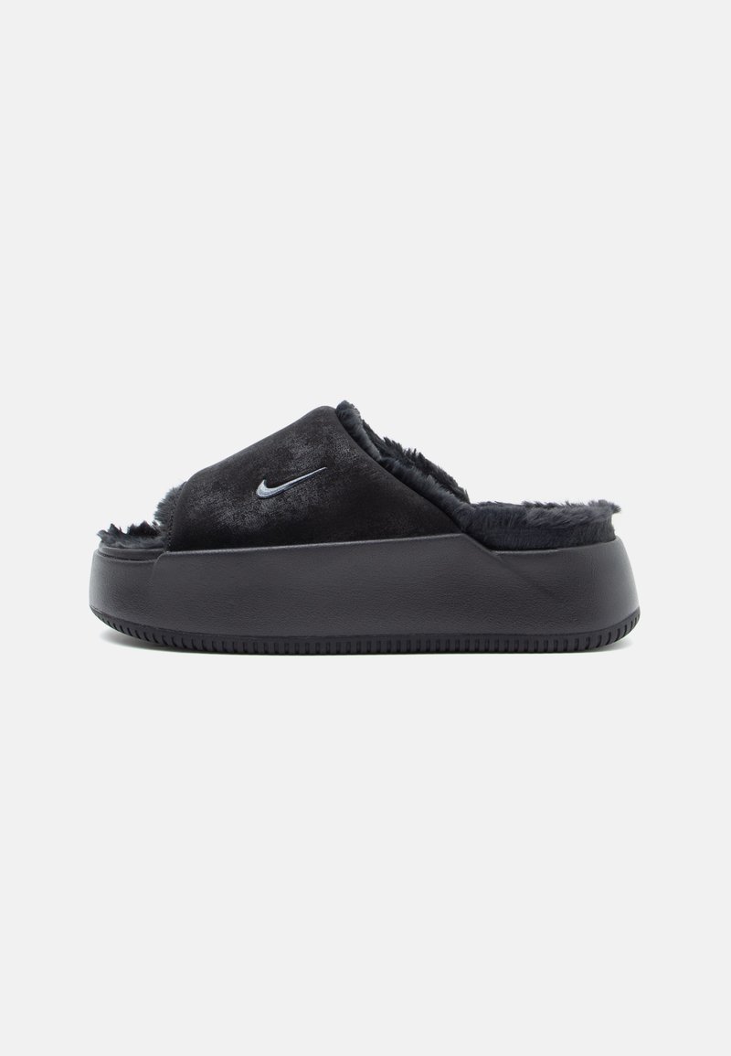 Zapatillas deslizantes negras con un forro de pelaje suave y una suela de goma texturizada, con un pequeño logo plateado de Nike en la parte superior.