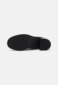 Semelle de chaussure noire avec surface texturée, présentant des rainures horizontales et un talon bloc. Le matériau semble être du caoutchouc avec un léger éclat.