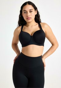 Svart formad kup-bh med breda justerbara remmar, slätt tyg, stödjande design och sömlös finish. Matchad med högmidjade svarta leggings.