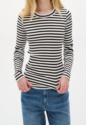 Haut à rayures noires et blanches à manches longues en rib, avec un col rond, associé à un jean en denim bleu. Main visible sur l'ourlet.