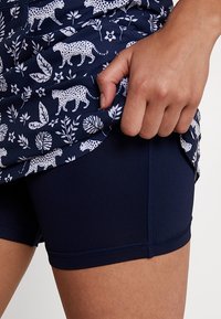 Námořnické šortky s hladkou texturou, spárované s topem s květinovým a zvířecím vzorem, zahrnujícím bílé levharty a listy.