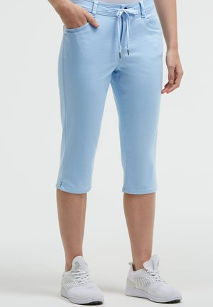 Light blue knee-length pants with drawstring waist worn with white athletic shoes, one hand in pocket, standing on white background.