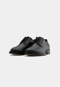 Chaussures en cuir noir avec un bout arrondi, un design à lacets, une tige minimaliste et une semelle plate en caoutchouc. Texture lisse et lignes épurées.