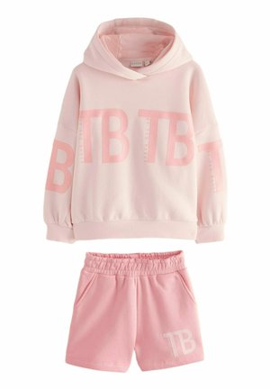 Conjunto de sudadera y pantalones cortos rosa. La sudadera tiene capucha y mangas anchas, con letras grandes de color rosa claro. Los pantalones cortos tienen una cinturilla elástica.