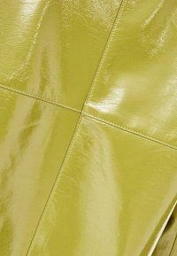 Glanzend, gestructureerd materiaal in fel limoengroen met zichtbare stiksels. Heeft een geometrisch patroon gevormd door paneelsecties.