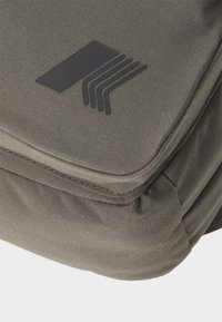 Sac en tissu gris foncé avec une texture lisse et un logo noir composé de trois lignes horizontales sur le rabat avant. Design compact.