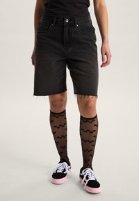 Pantalones cortos de mezclilla negra con dobladillo deshilachado, combinados con medias negras transparentes hasta la rodilla con un patrón geométrico y zapatillas negras y rosas.