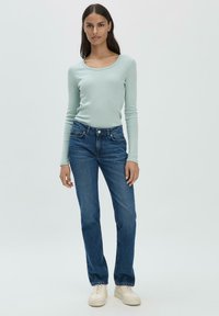 Top a maniche lunghe azzurro chiaro abbinato a jeans scuri a gamba dritta. L'outfit è completato da sneakers color crema.