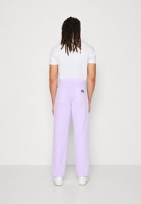 Fialové kalhoty vyrobené z bavlny, s rovnými nohavicemi, zadními kapsami a štítkem na pase. Kombinované s bílým tričkem a teniskami.