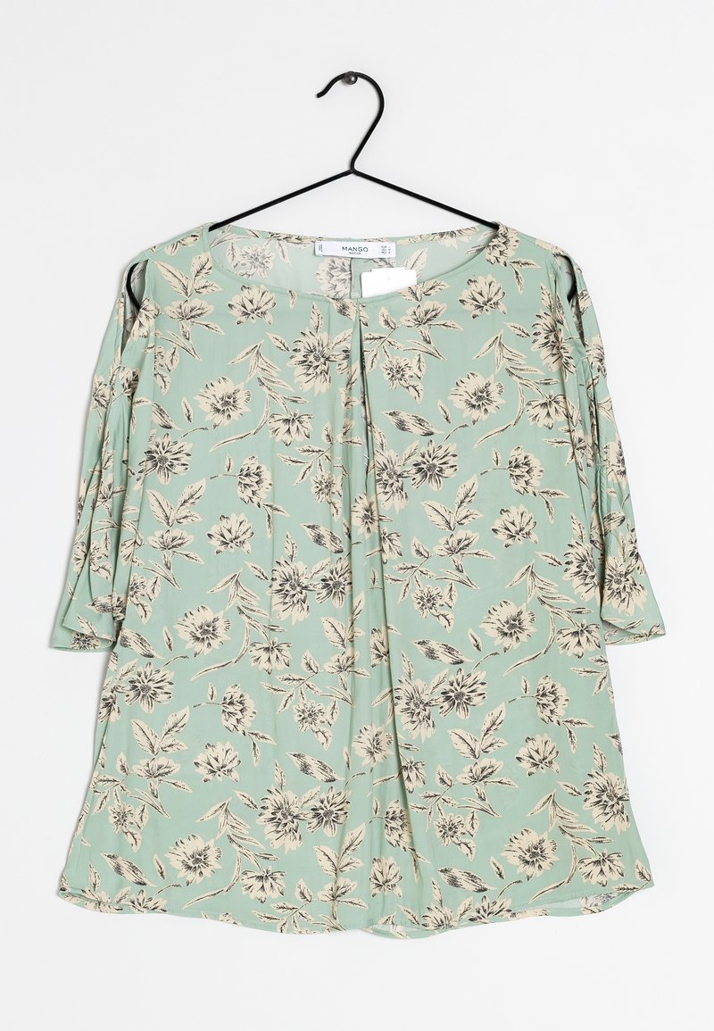 Blouse vert clair avec motif floral noir et blanc, manches trois-quarts et encolure ronde, suspendue sur un cintre noir.