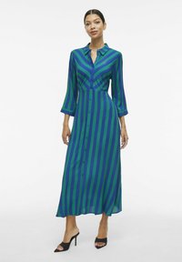 Dolga obleka s sprednjim gumbom, v zelenih in modrih navpičnih črtah, ovratnikom in rokavi do tri četrt. Gladek material s tekočim krojem.