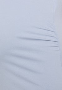 Světle modrý přiléhavý top vyrobený z úpletu. Obsahuje mírné skládání na boku pro zvýšení textury. Hladký povrch s jemným zakončením.