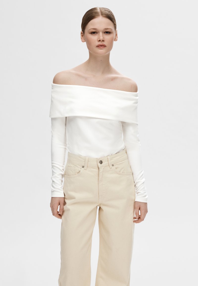 Off-shoulder hvit topp med lange ermer, kombinert med beige høyt liv brede bukser, med knappestolpe foran og sidelommer.