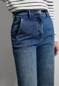 Pantalones de mezclilla azul con un diseño de talle alto y pierna recta, y un sutil degradado de color de denim claro a oscuro. Dos bolsillos laterales visibles.