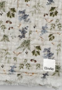 Bomuld muslin tæppe med en lys beige bund, prydet med grønne og blå botaniske print. Kantet med blød, frynset tekstur. Brandmærke synligt.
