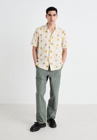 Short-sleeve, light beige shirt with fruit patterns; paired with light green cargo pants. Black shoes with thick soles.