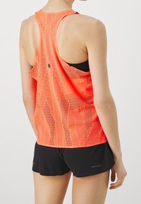 Leichtes, hellorangefarbenes Mesh-Top mit Racerback-Design, das ein strukturiertes Muster und belüftete Bereiche für Atmungsaktivität aufweist. Schwarze Shorts.