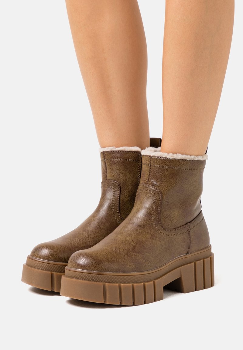 Brązowe skórzane botki za kostkę o teksturowanym wykończeniu, z puszystym kremowym wykończeniem przy kołnierzu i masywną, żebrowaną gumową podeszwą.