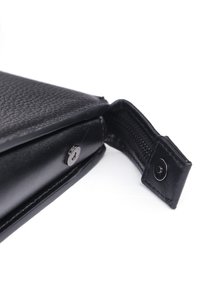 Sort læderpung med en tekstureret overflade, udstyret med en sølv trykknaplukning og en lynlås, delvist åben for at vise indersiden.