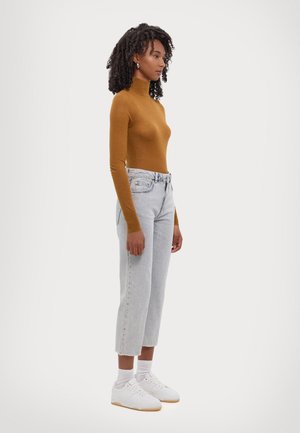 Brun, tettsittende turtleneck-genser, kombinert med lyse, høytlivde, rette jeans. Hvite joggesko og ankelsokker fullfører antrekket.