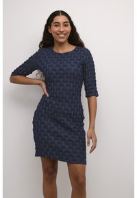 Mörkblå klänning med ett strukturerat vävat mönster, trekvartslånga ärmar och en figursydd silhuett som når mitt på låret. Slät tygfinish.