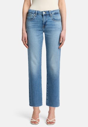 Jean droit bleu clair en denim, avec un délavage vieilli, un design à cinq poches et un ourlet effiloché, associé à des sandales blanches à lanières.