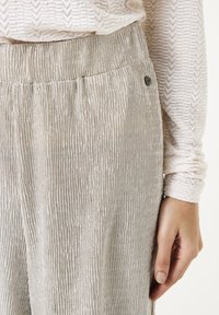 Lichtgrijze textuurbroek met een verticale ribbelpatroon, voorzien van een gladde tailleband en een klein merkaccent aan de zijkant.