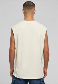Lys beige ærmeløs top med en afslappet pasform, lavet af blødt stof. Har en rund hals og en buet kant, designet til komfort.