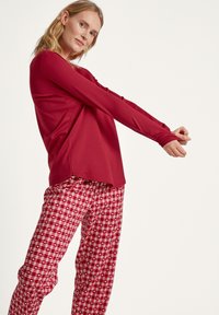 Rotes Langarmshirt mit abgerundetem Saum, kombiniert mit rot-weißen karierten Schlafanzughosen mit Herzmuster, aus weichem Stoff gefertigt.