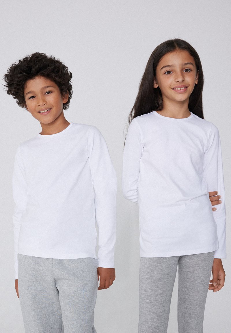 Zwei Kinder tragen langärmlige weiße T-Shirts und graue Hosen. Der Stoff wirkt glatt, mit einem einfachen Rundhalsausschnitt und ohne sichtbare Muster.