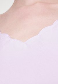 Zbliżenie na jasnofioletowy strój z falbaniastym dekoltem noszony na odsłoniętej skórze.