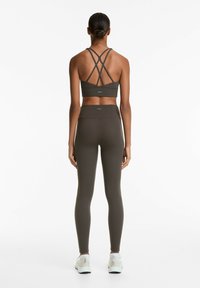 Donker olijfgroene sportbh met kruisbanden en bijpassende high-waisted legging, beide gemaakt van glad, rekbaar materiaal. Witte sneakers inbegrepen.