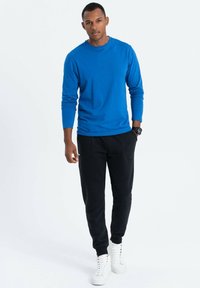 Blauwe t-shirt met lange mouwen en zwarte joggers, met zijzakken, gecombineerd met witte sneakers. Eenvoudig, modern ontwerp en zachte textuur.