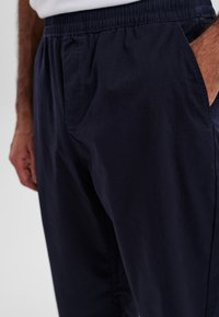 Marineblå, letvægts bomuldsbukser med elastisk talje, sidelommer og løs pasform, der har en glat tekstur.