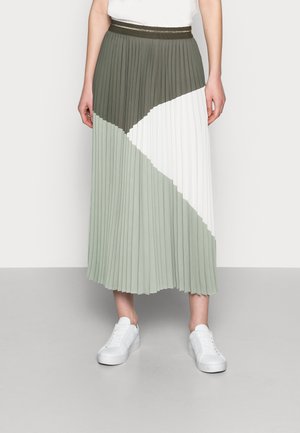 Jupe midi plissée avec des blocs de couleurs diagonaux en olive foncé, blanc et sauge claire, portée avec des baskets blanches sur une personne debout.