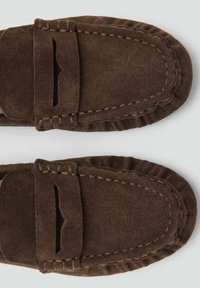 Mocassins en daim marron avec un design cousu, présentant un accent en découpe sur le dessus et un bout arrondi. Texture douce et forme flexible.