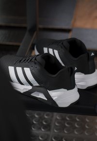 Black athletic shoes with white stripes, textured upper, padded collar, and thick white sole. Features a TPU heel counter for support.