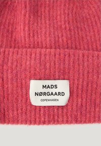 Knitted beanie in a vibrant pink color with horizontal ribbed texture. Features a white label with "MADS NØRGAARD COPENHAGEN" in black.
