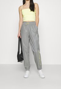 Graue, leichte Nylon-Jogginghosen mit elastischem Bund und verstellbarem Kordelzug, ausgestattet mit einem neon-gelben Markenlogo an der linken Beinschine.