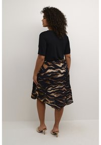 Top negro de manga corta combinado con una falda fluida con un patrón de olas marrón y beige sobre un fondo oscuro. Textura suave, ajuste relajado.