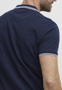 Tengerészkék póló fehér csíkozott gallérral és ujjamintákkal, texturált anyagból készült, standard szabású és egyszínű kialakítással.