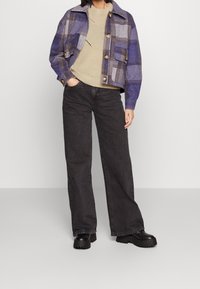 Rutig jacka i lila och grått, med guldknappar och två framfickor, kombinerad med en beige stickad tröja och svarta vida jeans.