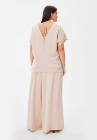 Beige tweedelig outfit met een loszittend topje met korte mouwen en open rugdetail, gecombineerd met wijde broekspijpen. Gladde textuur.