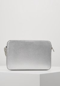 Bolso cruzado rectangular plateado con superficie texturizada, bordes redondeados, cierre de cremallera y una corta correa de cadena plateada sobre un fondo neutro.